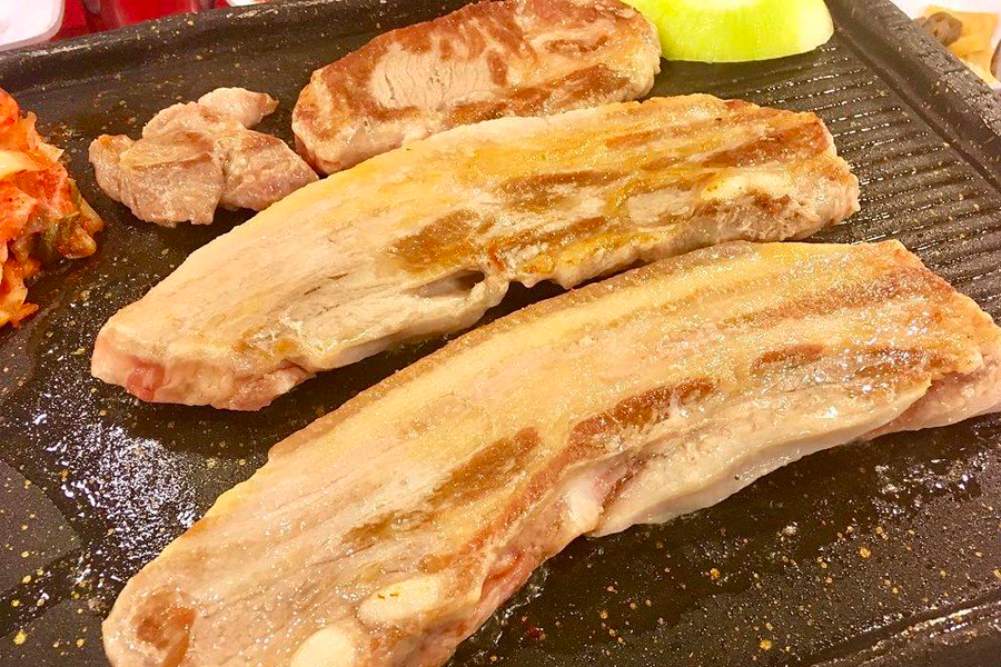 Fresh slices of 삼겹살 sizzling on a grill with accompanying dishes like kimchi