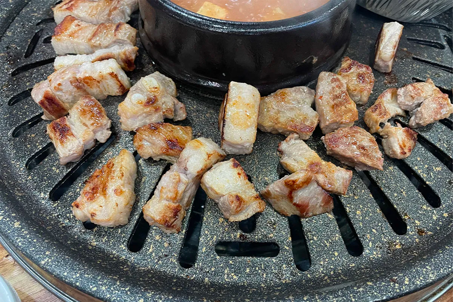 Thin and crispy 갈치조림 and pork belly strips on a grill being prepared in a Korean BBQ setting
