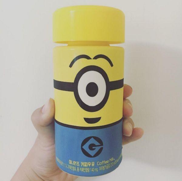 手握小黄人咖啡牛奶瓶，背景是白色墙壁，瓶身印有小黄人Bob的微笑表情。