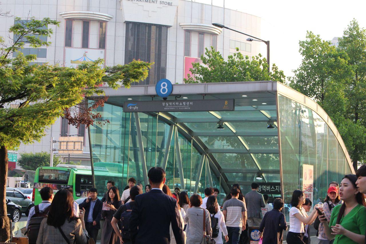 蚕室地铁站入口，旁边有树木与购物中心，是游览蚕室的起点。