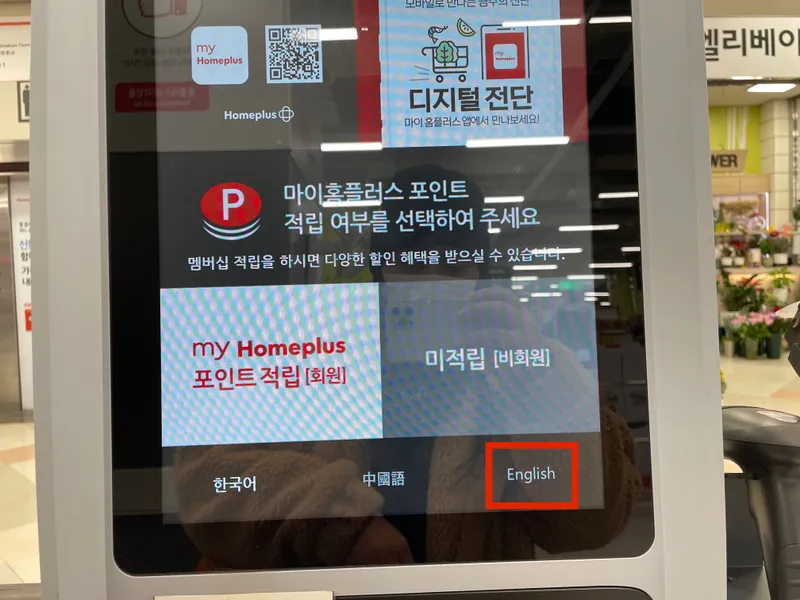 Close-up view of a self-service checkout kiosk at Homeplus Seoul, highlighting language options in Korean, Chinese, and English, designed for user convenience.