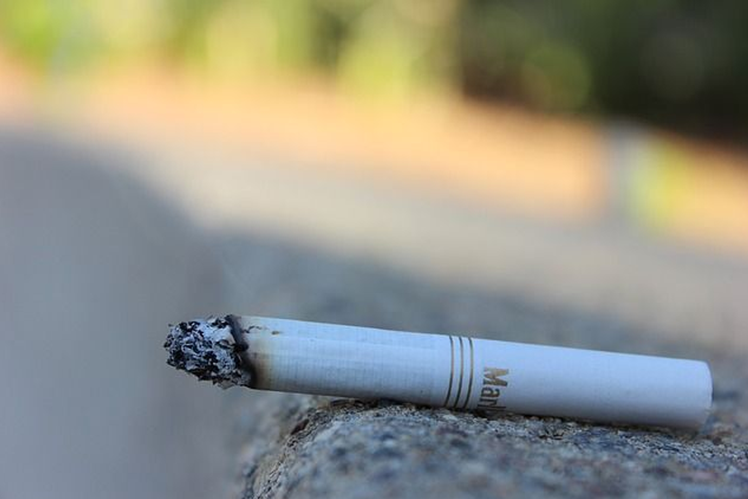 點燃的香煙，放置於户外的木桌上，背景模糊。