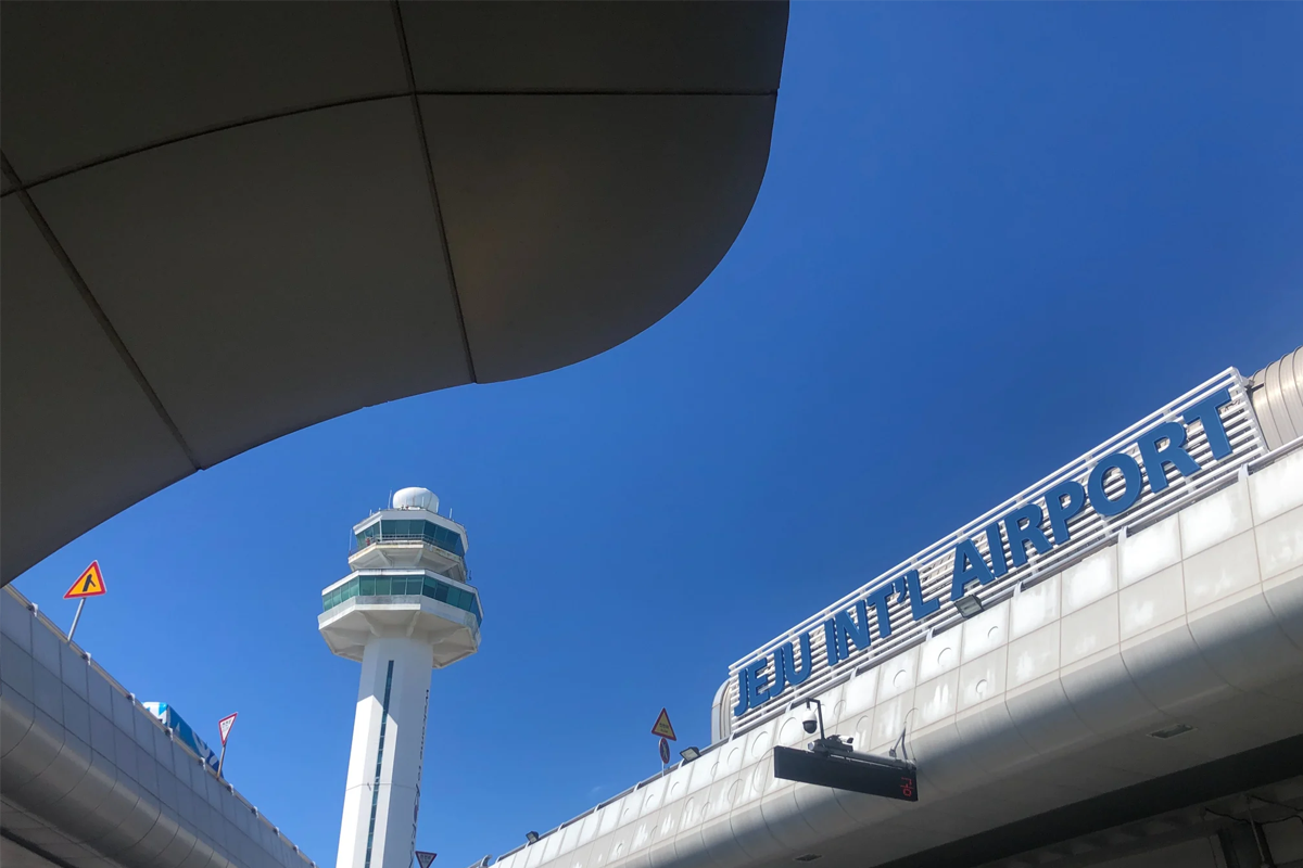 A view of Jeju International Airport showcasing the airport's architecture and air traffic control tower against a clear blue sky, highlighting its accessibility and location.