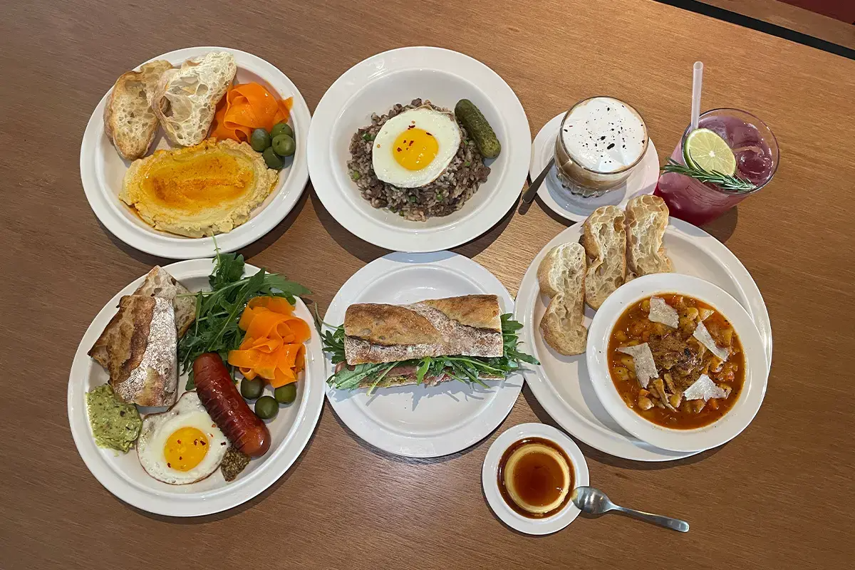 A delectable spread at Furoa Cafe featuring a brunch plate, bulgogi pilaf, basil butter arugula sandwich, soup of the day, and Furoa Coffee served elegantly on white plates.