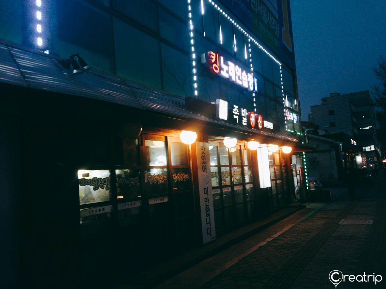 The exterior of the Jokbal restaurant '족발귀신', lit up with neon lights, showcasing a retro Korean atmosphere.