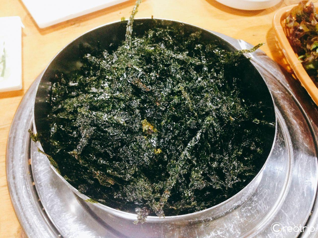 A customer at Jokbal restaurant holding a garlic and sauce-covered pork wrapped in fresh lettuce.