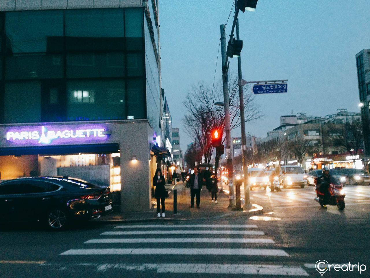 A bustling street scene in Seoul with a Paris Baguette store, on the way to Jokbal restaurant at night.