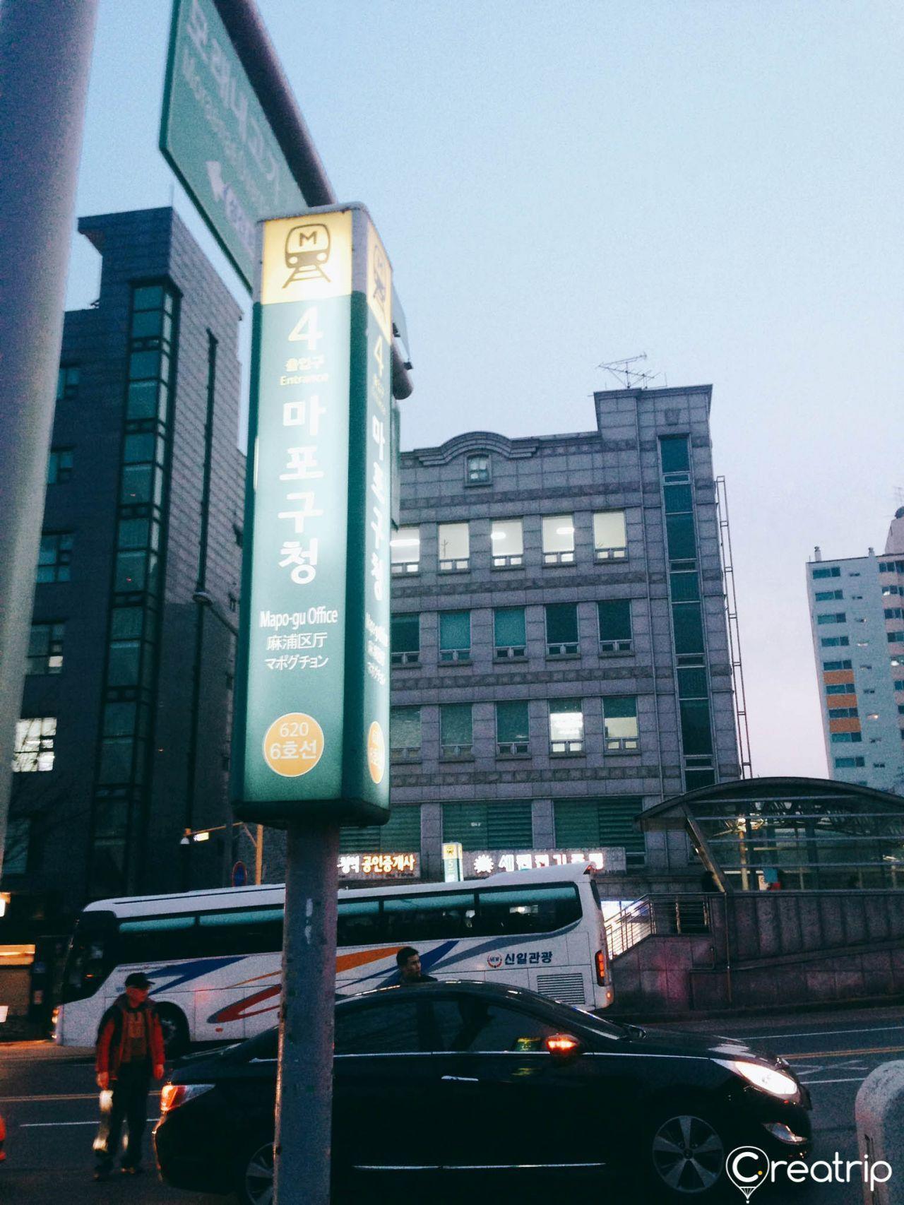 A tall sign outside Mapo-gu Office station, showing the subway stop and entrance number 4, near Jokbal restaurant in Seoul.