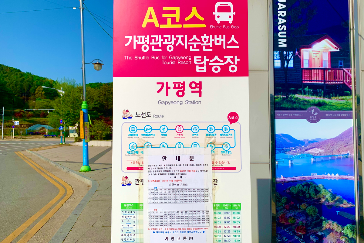 ป้ายจอดรถแท็กซี่หน้าสถานี Gapyeong บนเกาะนามิ, เกาหลี. ป้ายสีชมพูแสดงเส้นทางและตารางเวลาของรถบัส. สภาพอากาศแจ่มใสและมีทิวทัศน์ธรรมชาติในฉากพื้นหลัง.