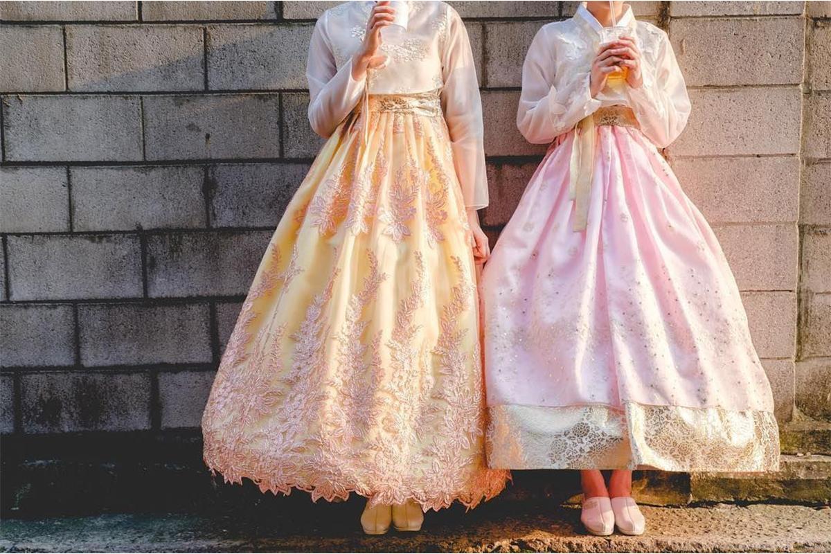 穿著韓服的顧客拍攝於傳統韓國建築前,背景是綠樹成蔭的庭院,呈現出悠閒的韓國之旅氛圍.