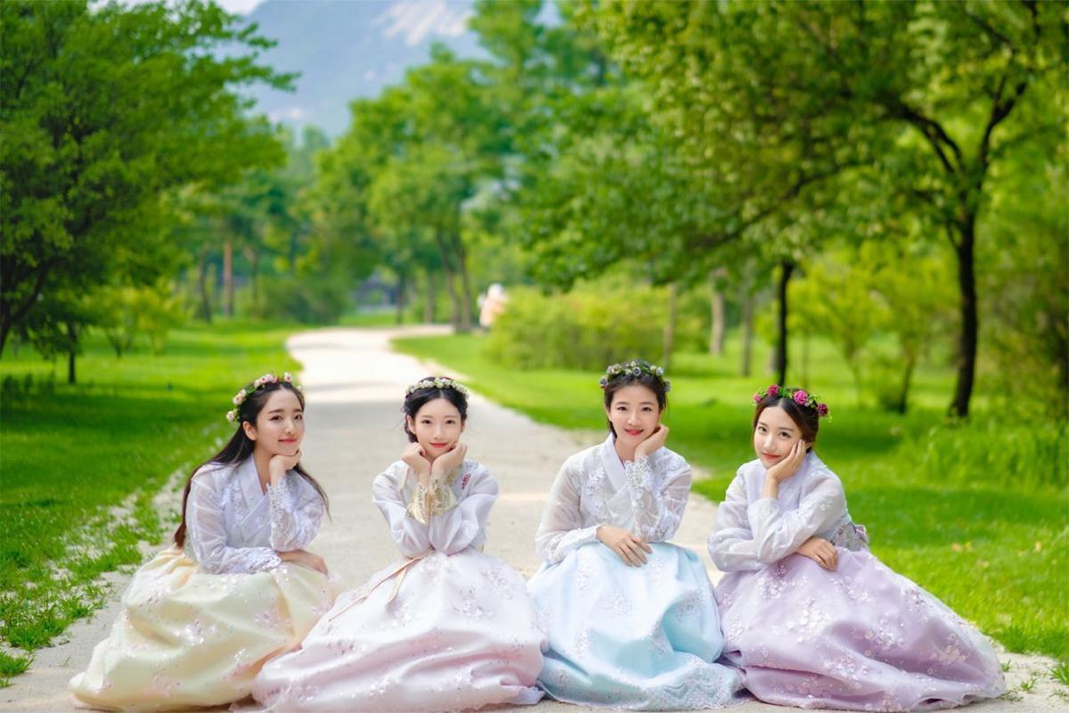 顧客穿著粉紅色和黃色韓服站在石牆前,顯示出韓服的美麗和細膩的刺繡設計.