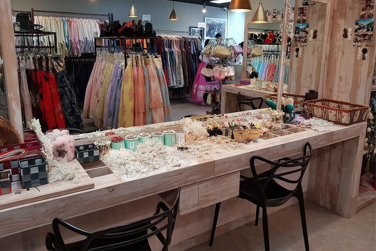 展示區掛滿各式精緻韓服,牆邊的鏡子前有一張小桌,上面放著一些日常的美容小工具和裝飾品.