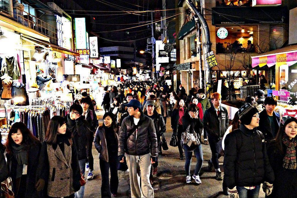 弘大购物街的熙攘人群，众多购物者穿梭于商店之间，凸显地区的活力和热闹。