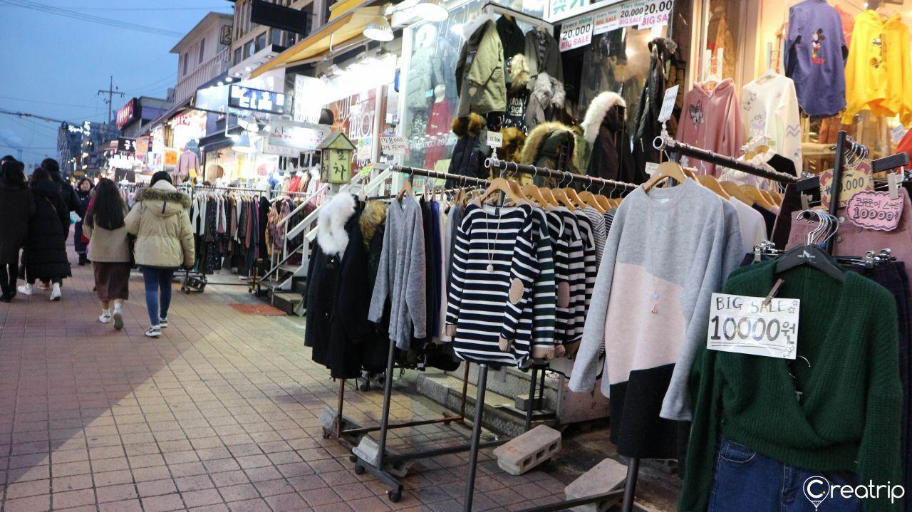 弘大购物街上出售中和打折的时尚服装，吸引购物者选购。