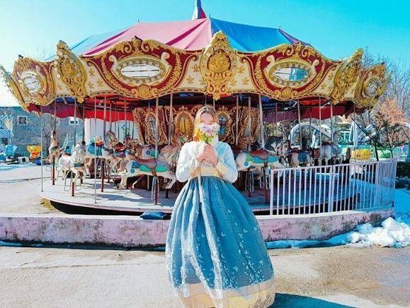 용마랜드의 회전목마 앞에서 한복을 입은 사람이 서 있는 모습입니다.