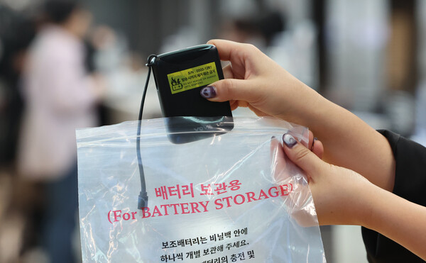 Person holding battery storage pack with text indicating airline restrictions on carrying power banks, representing Korea's new aviation regulations.