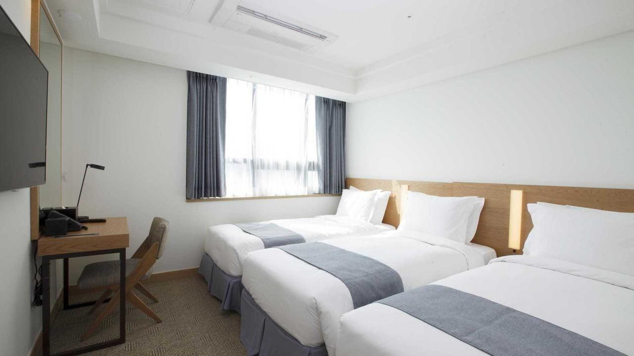 现代化酒店房间内部，配有三张双人床和简单的家具设计，适合舒适住宿。