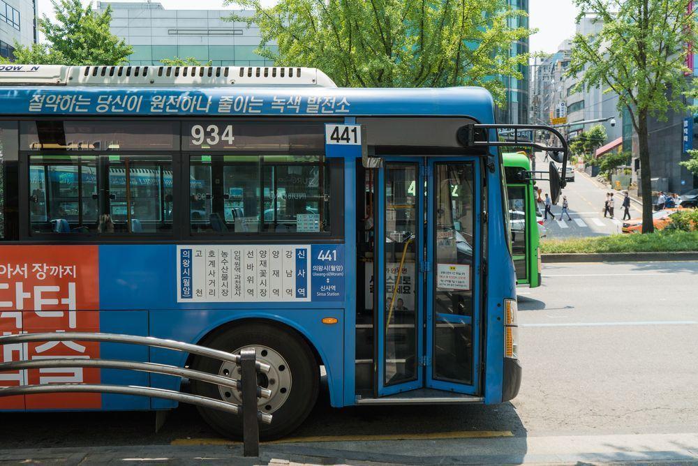 首尔街头的蓝色公交巴士，行驶路线和乘客进出车门的日常场景。