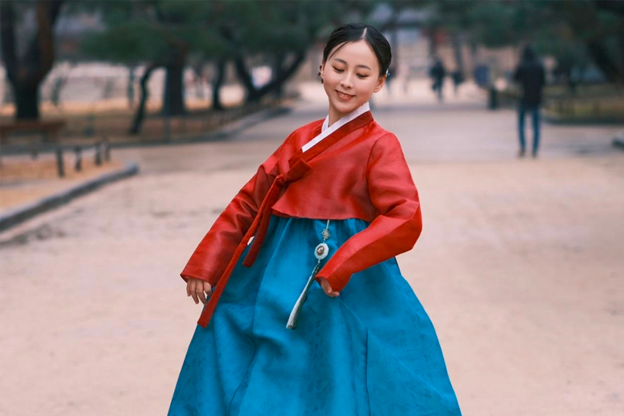 Red and blue hanbok worn by a person with blurred face, showcasing traditional Korean attire.