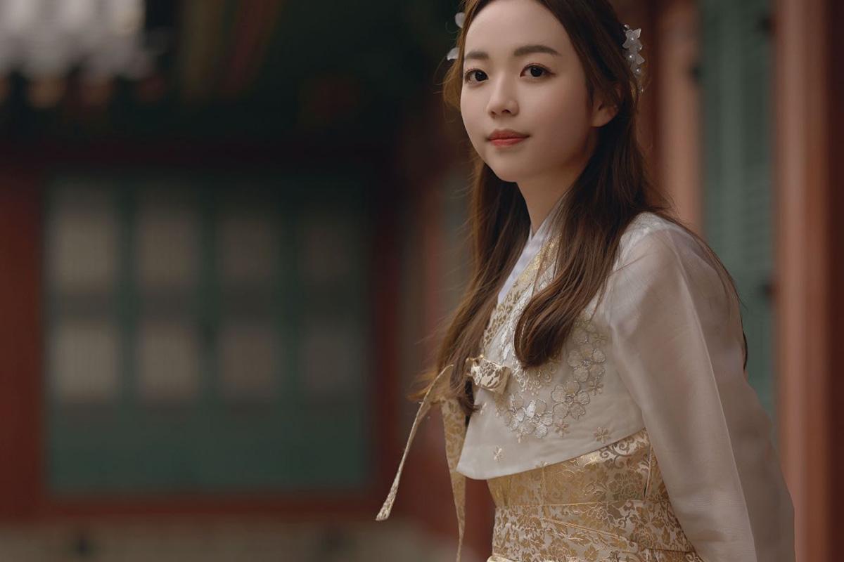 身穿白色韓服的公主風格女生站在古樸建築前,展現優雅風采。