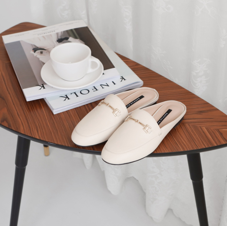 Off-white leather loafers displayed on a coffee table next to magazines and a coffee cup, showcasing SAPPUN's stylish home footwear.