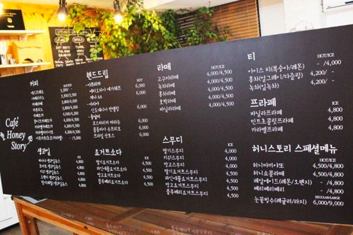 黑板上有詳細的咖啡館菜單，包括咖啡、飲品與甜品選擇，旁邊裝飾有植物，營造舒適的咖啡館氛圍。