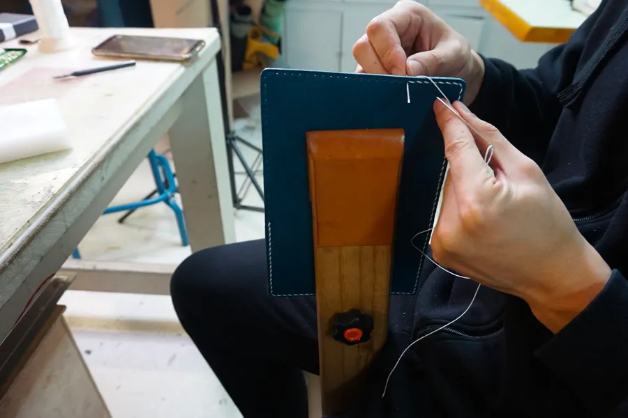 Participant stitching leather craft item in Korean leather DIY workshop, focusing on craftsmanship and durability.