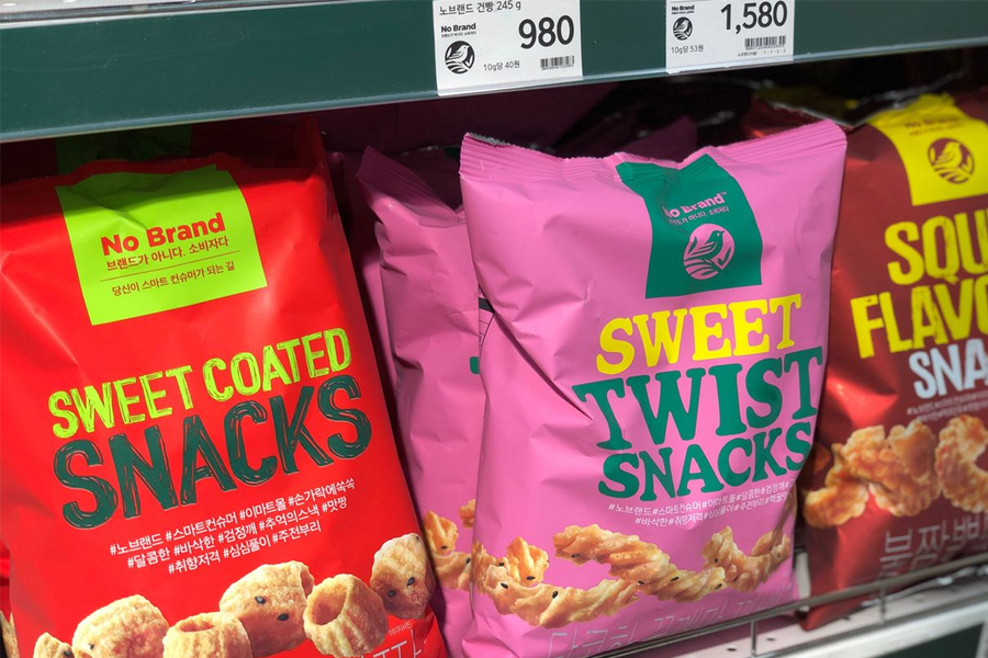 Brightly colored No Brand snack bags on a retail shelf. The signature eye-catching packaging of No Brand snacks, including sweet coated and sweet twist variations, emphasize the variety available for snack lovers.