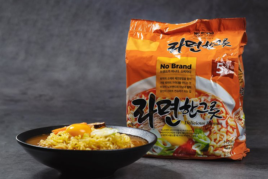 No Brand spicy noodle package next to a bowl of prepared ramen with an appetizing egg on top. The packaging highlights the vibrant and bold flavors expected in classic Korean instant noodles.