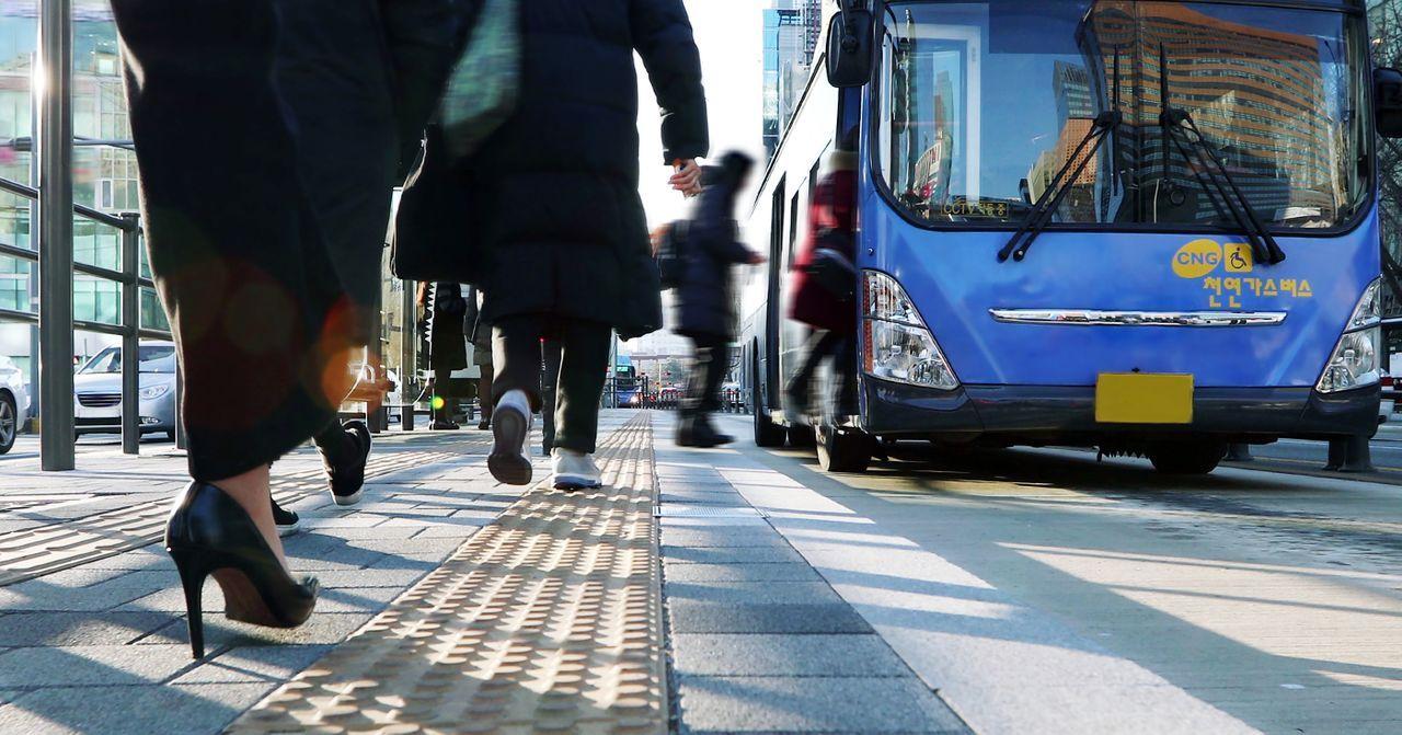 人们在拥挤的城市步道上行走，背景中可见蓝色公共汽车。