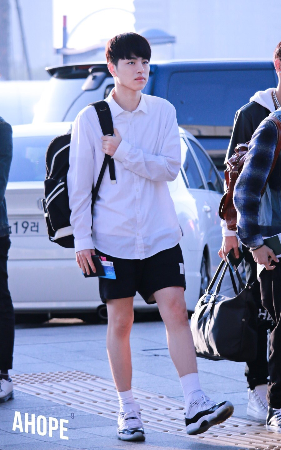 一位年轻男性穿着白衬衫和超短裤，搭配运动鞋，走在户外街道。