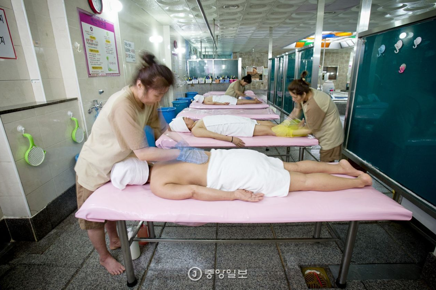 在韓國汗蒸幕中，一位專業技師正在為顧客搓澡，這種服務對去死皮和放鬆身心非常有效，是韓國獨有的洗浴文化。