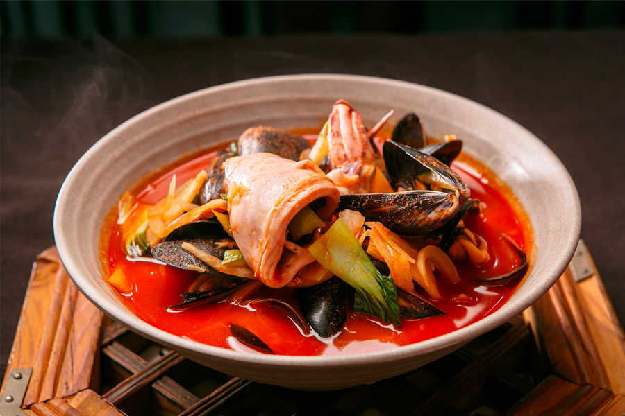 一碗熱騰騰的韓式辣海鮮麵，充滿豐富的海鮮如鮮蝦和貝類，浸在辣味湯頭中，視覺上顯得紅火且誘人，讓人垂涎欲滴。