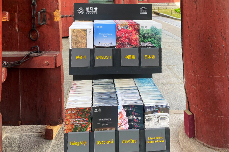 Rack of multilingual brochures at Changdeokgung Palace entrance, offering cultural information.