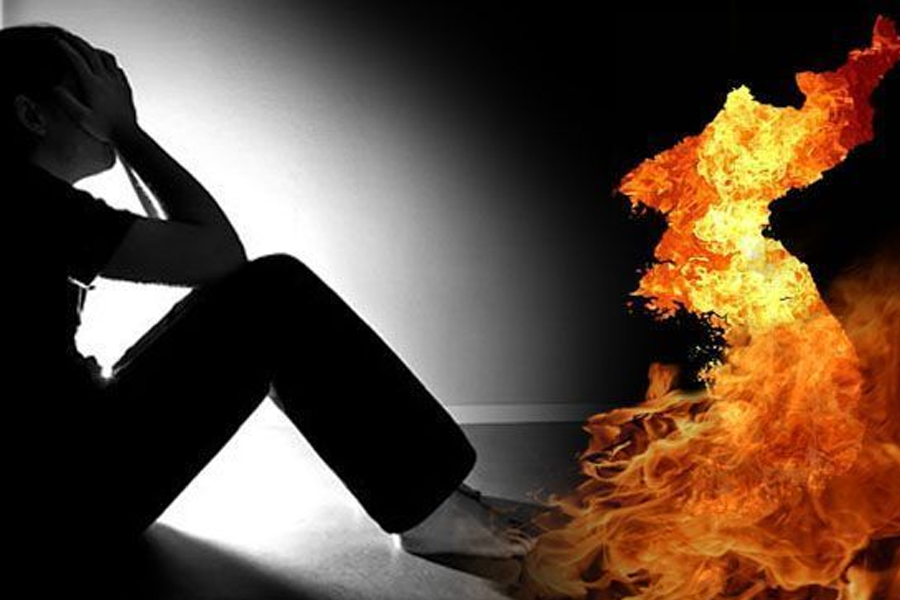 A person sitting in the dark next to a burning map of Korea, symbolizing the stress and pressures faced by youth in South Korea.