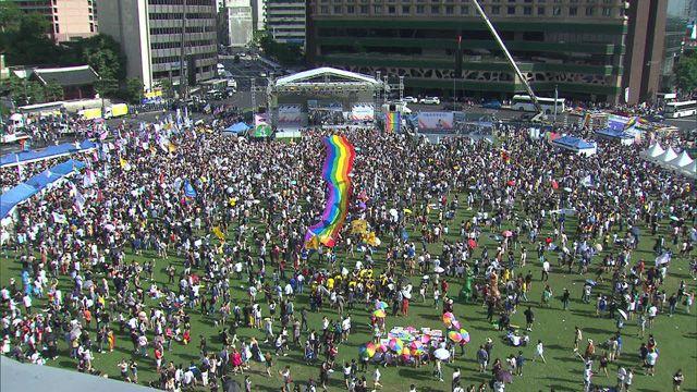 在户外廣場上舉行的盛大的LGBTQ+活動，彩虹旗在人羣中顯眼地展示著。