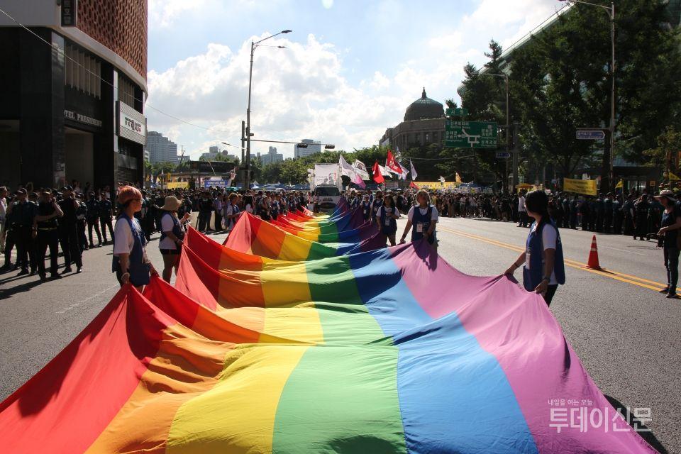 大型LGBTQ+遊行中展開巨型彩虹旗，顯示平等的支持與包容。