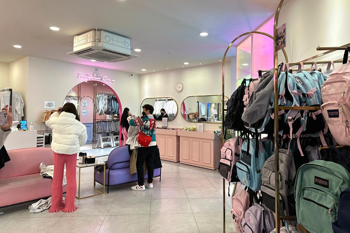 Button-up shirts and skirts neatly folded and organized in a pastel-themed room inside Ehwa School Uniform rental shop.