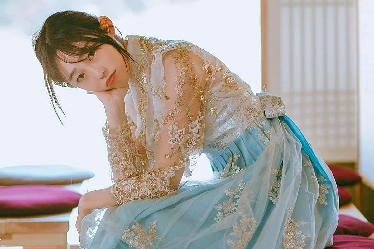 身穿黑色刺繡罩衫的女子站在韓屋裡，展示韓服的細緻刺繡與華麗設計。」