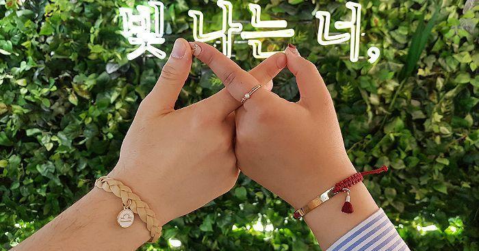 Close-up of hands displaying friendship bracelets against a lush green backdrop with Korean text.