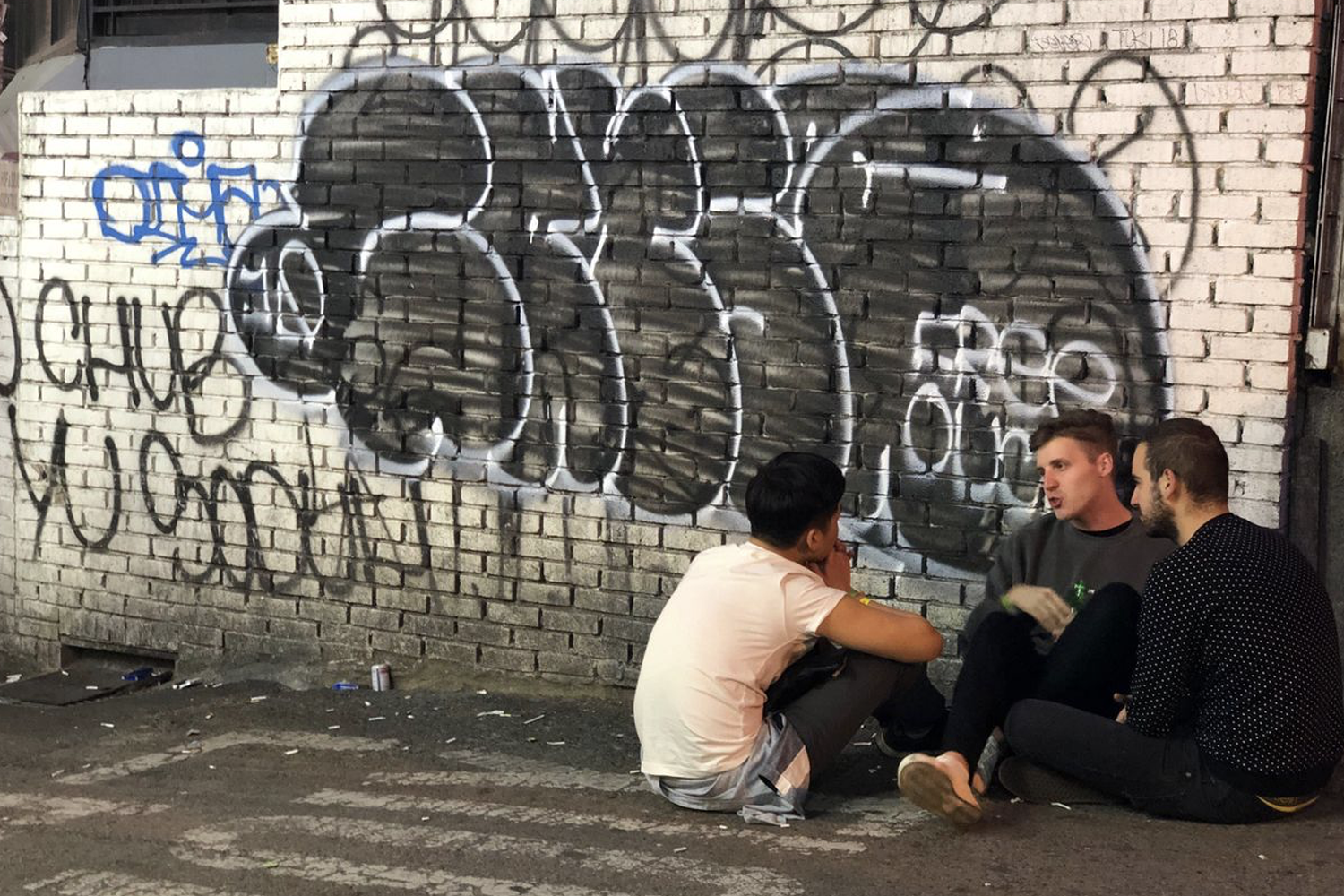三名男子聚集於牆邊討論生活於自由風格塗鴉前