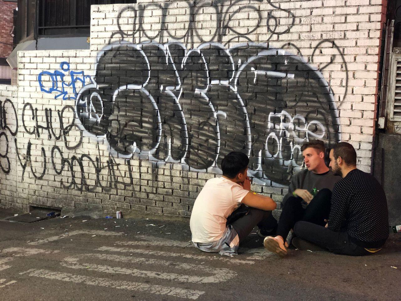 A group of people engaged in conversation beside a wall covered in graffiti, capturing an urban moment.