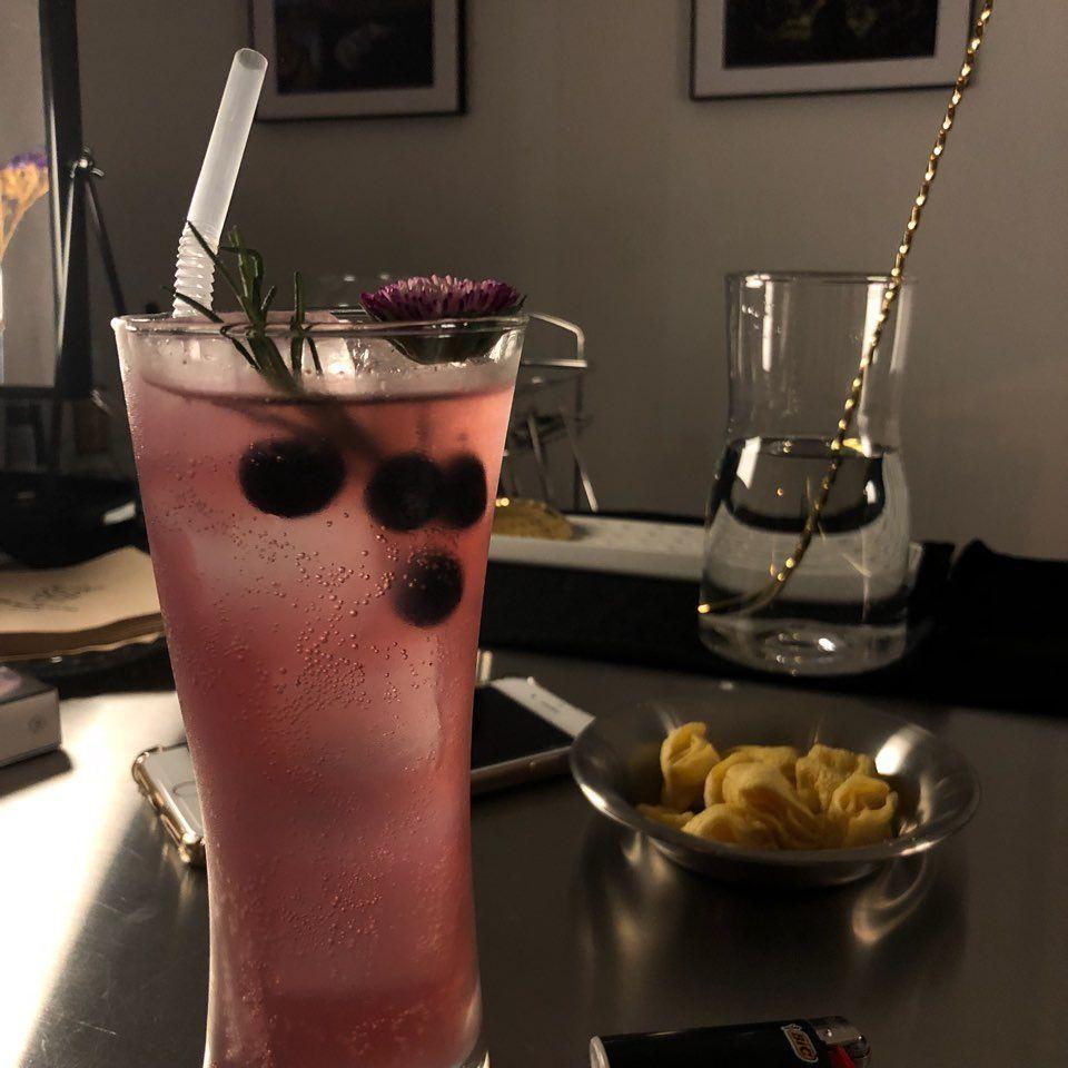 A refreshing pink cocktail drink garnished with berries and herbs served at a chic bar setting.