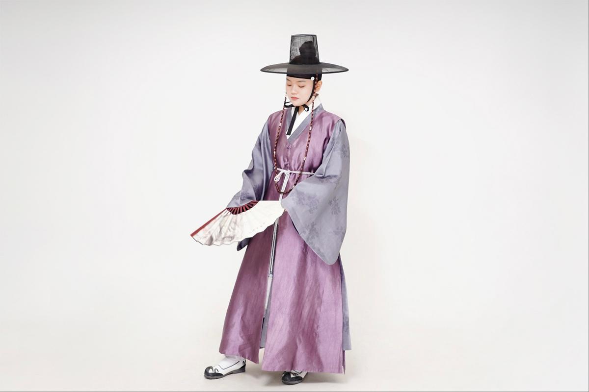 A person dressed in traditional Korean attire featuring a purple hanbok with intricate designs and traditional accessories.