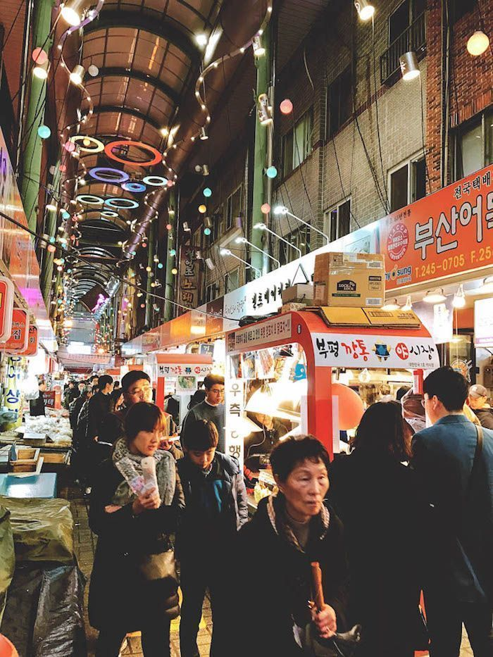 韓國某夜市內部，擺滿小販攤位和熙熙攘攘的人羣，體現夜市的繁忙與吸引力。