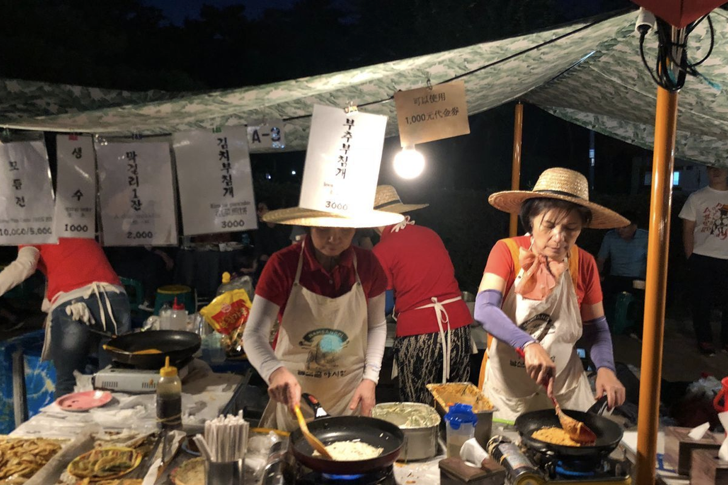 工作人員在韓式夜市攤位上烹飪傳統小吃，展示夜市的準備過程。