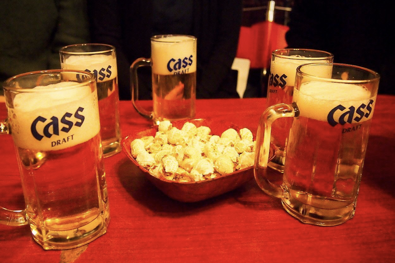 桌子上擺放著五杯Cass啤酒和一盤花生，營造夜市享受的隨意和放鬆氛圍。