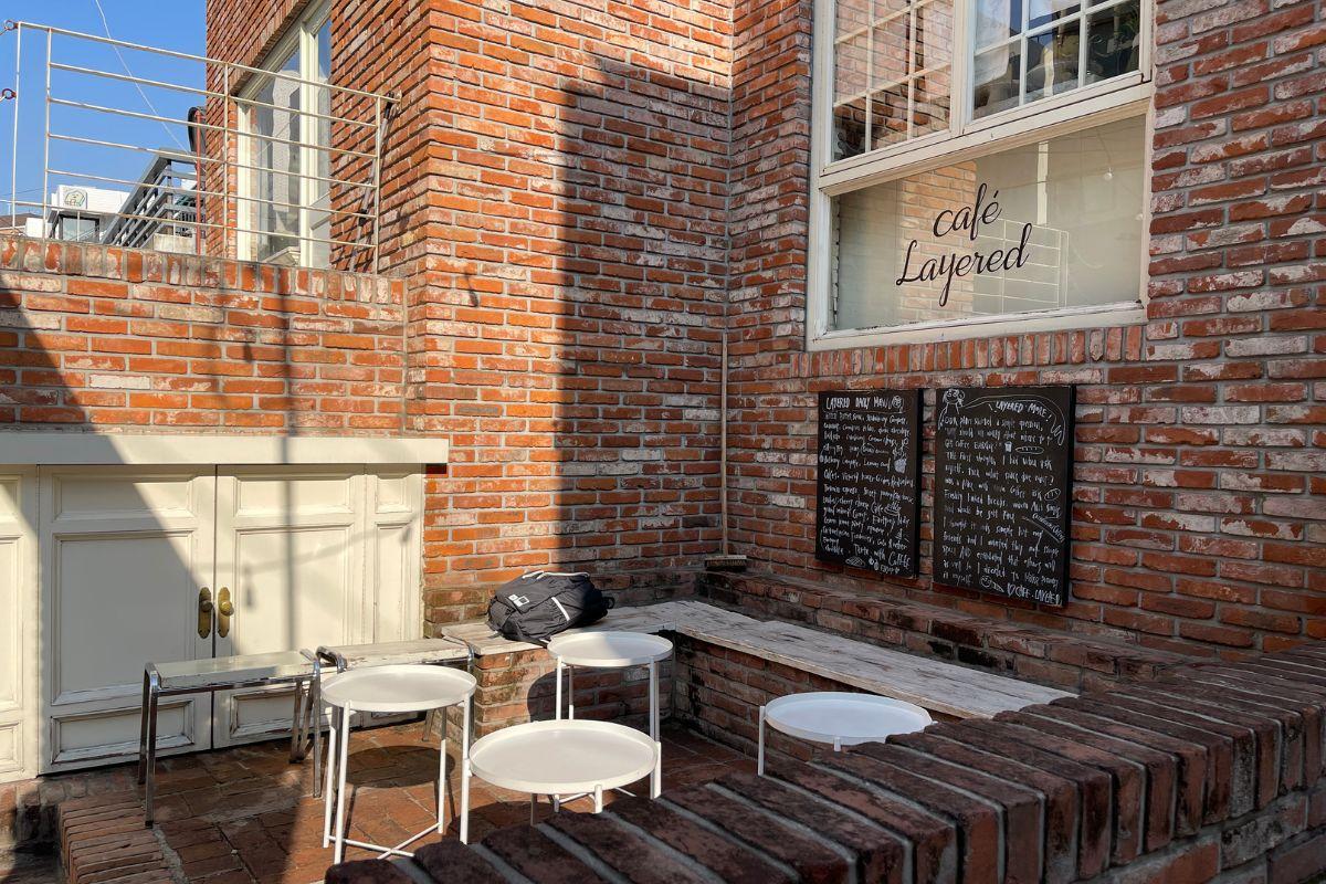 Exterior view of Cafe Layered in Yeonnam-dong featuring its distinctive brick wall and outdoor seating area with modern white chairs and tables.