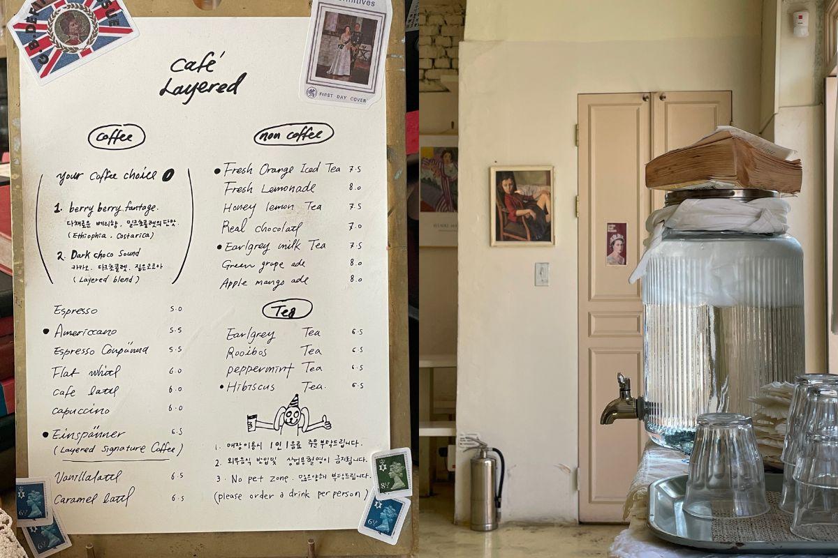 Interior menu board and a water dispenser at Cafe Layered, Yeonnam-dong, featuring a variety of coffee and tea options.