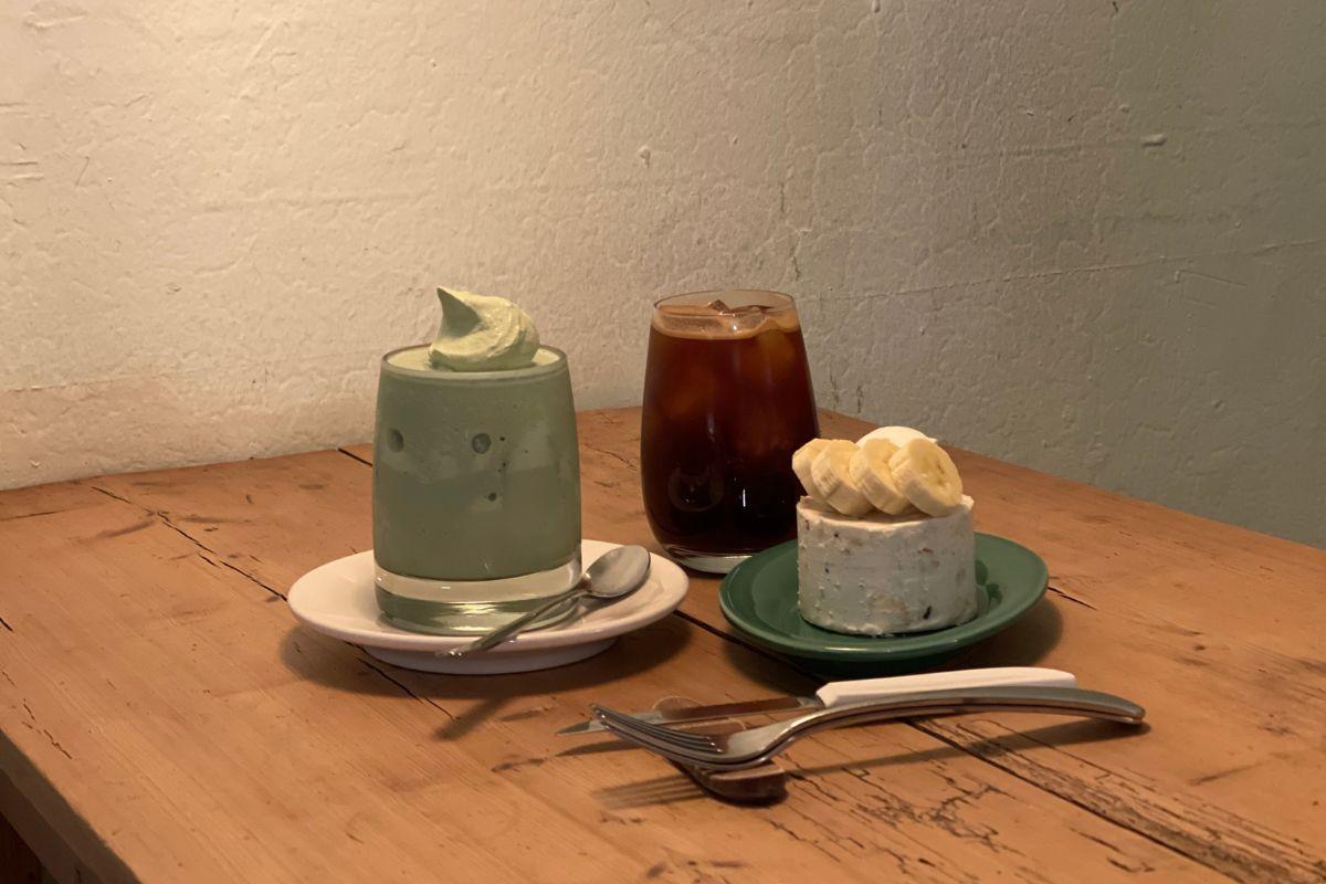Table at 'earth us' cafe in Yeonnam-dong showcasing an array of ordered items including a unique banana cheesecake and refreshing iced drinks.